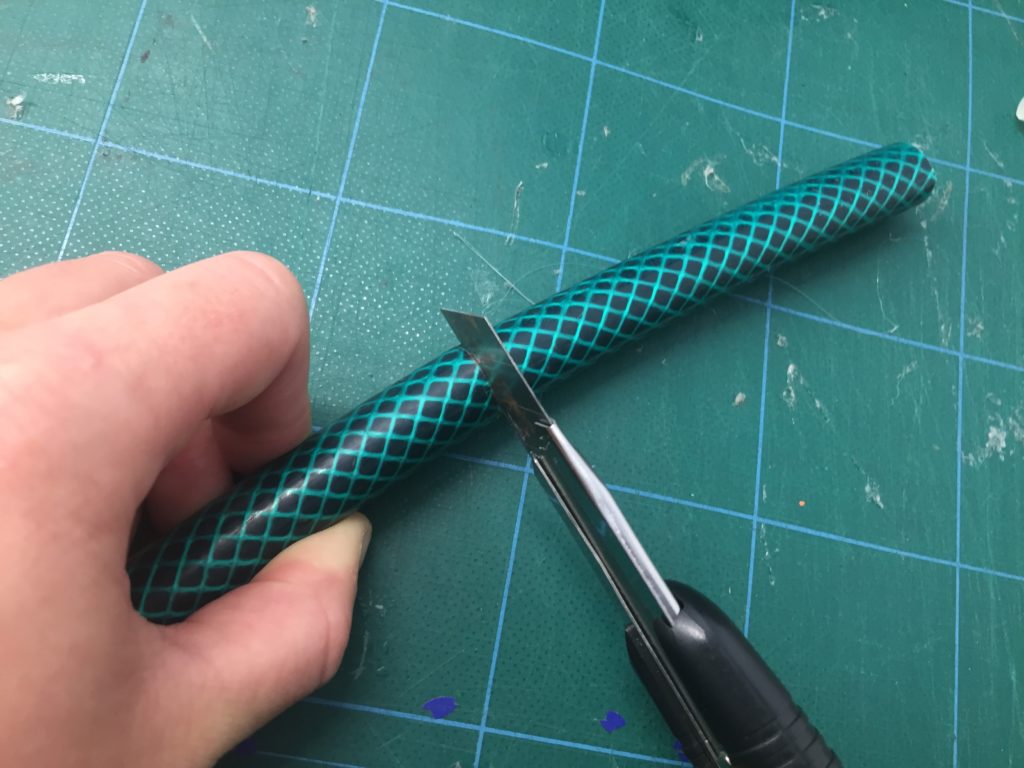 Image showing a garden hose being cut with a craft knife